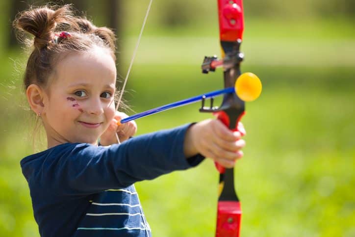 Linda niña arquera con arco disparando en soleado día de verano. Niña dispara con arco en el parque. Al aire libre. Actividades deportivas con niños. Concepto de deporte y estilo de vida. Apuntando alto