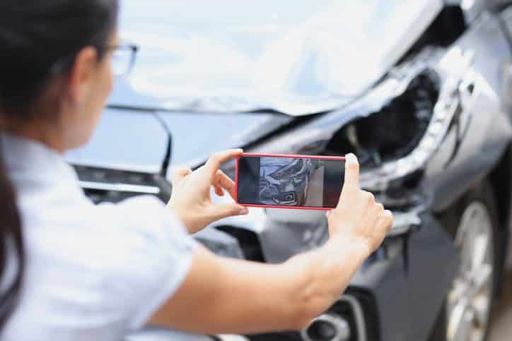 Insurance agent woman takes pictures by smartphone of car damage after road accident. Vehicle inspection and damage assessment concept