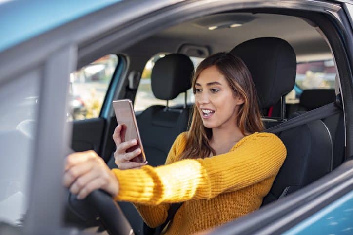 Enviar mensajes de texto y conducir, al volante. Incumplir la ley. Mujer conduciendo distraída por el móvil. Mujer escribiendo un mensaje en el teléfono mientras espera en el coche.