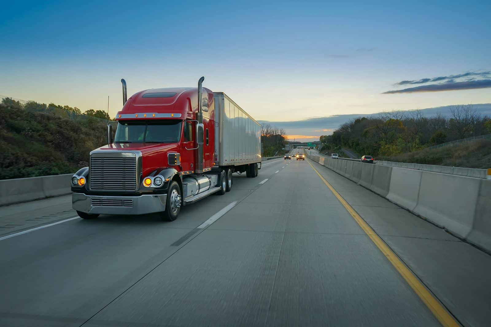 Red semi-truck tractor trailer 18 wheeler on highway at sunrise