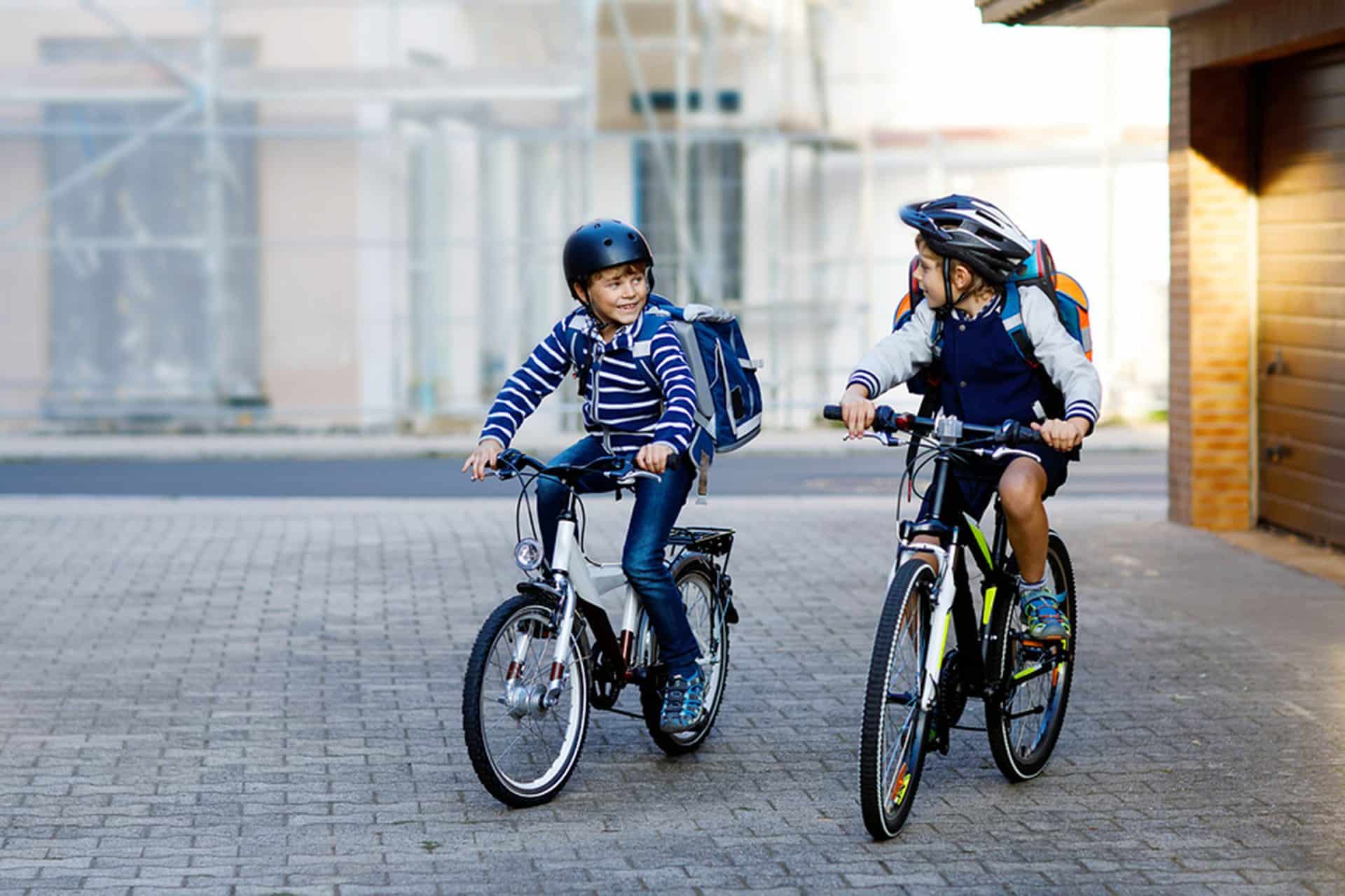 Two school kid boys in safety helmet riding with bike in the city with backpacks. Happy children in colorful clothes biking on bicycles on way to school. Safe way for kids outdoors to school